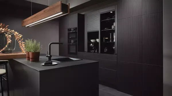 Moderne schwarze Designküche mit Kochinsel, Kräutertöpfen und eleganter Holzlampe.