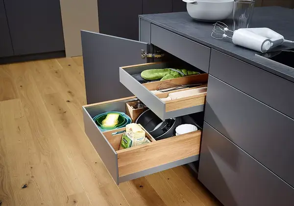 Moderne Küchenschubladen aus Holz und Grau, gefüllt mit Küchenutensilien und Lebensmitteln.