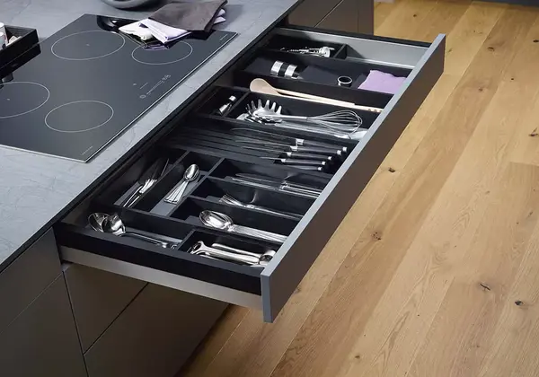 Offene Küchenschublade mit organisiertem Besteckkasten und Kochutensilien auf Holzfußboden.