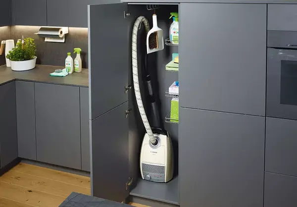 Staubsauger und Putzmittel ordentlich in einem modernen grauen Küchenschrank verstaut.