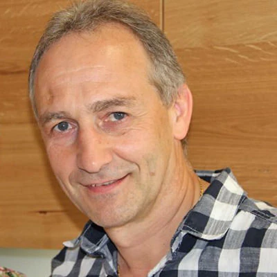 Porträt eines lächelnden Mannes in kariertem Hemd vor Holz-Wand, Profilbild