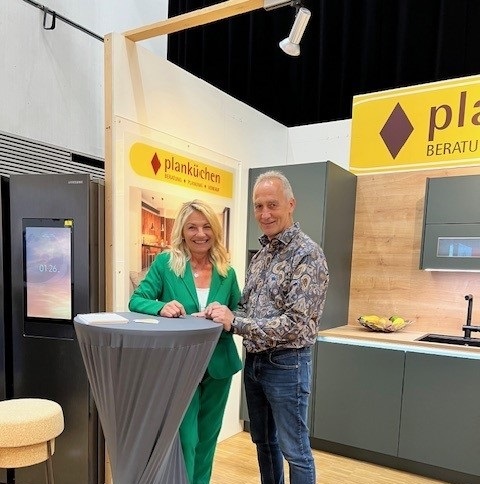 Zwei Personen stehen an einem Messestand von Planküchen mit moderner Küchenausstellung.