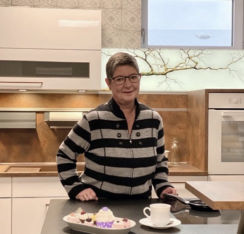 Eine Frau steht in moderner Küche mit Gebäck und Kaffee auf der Arbeitsplatte.